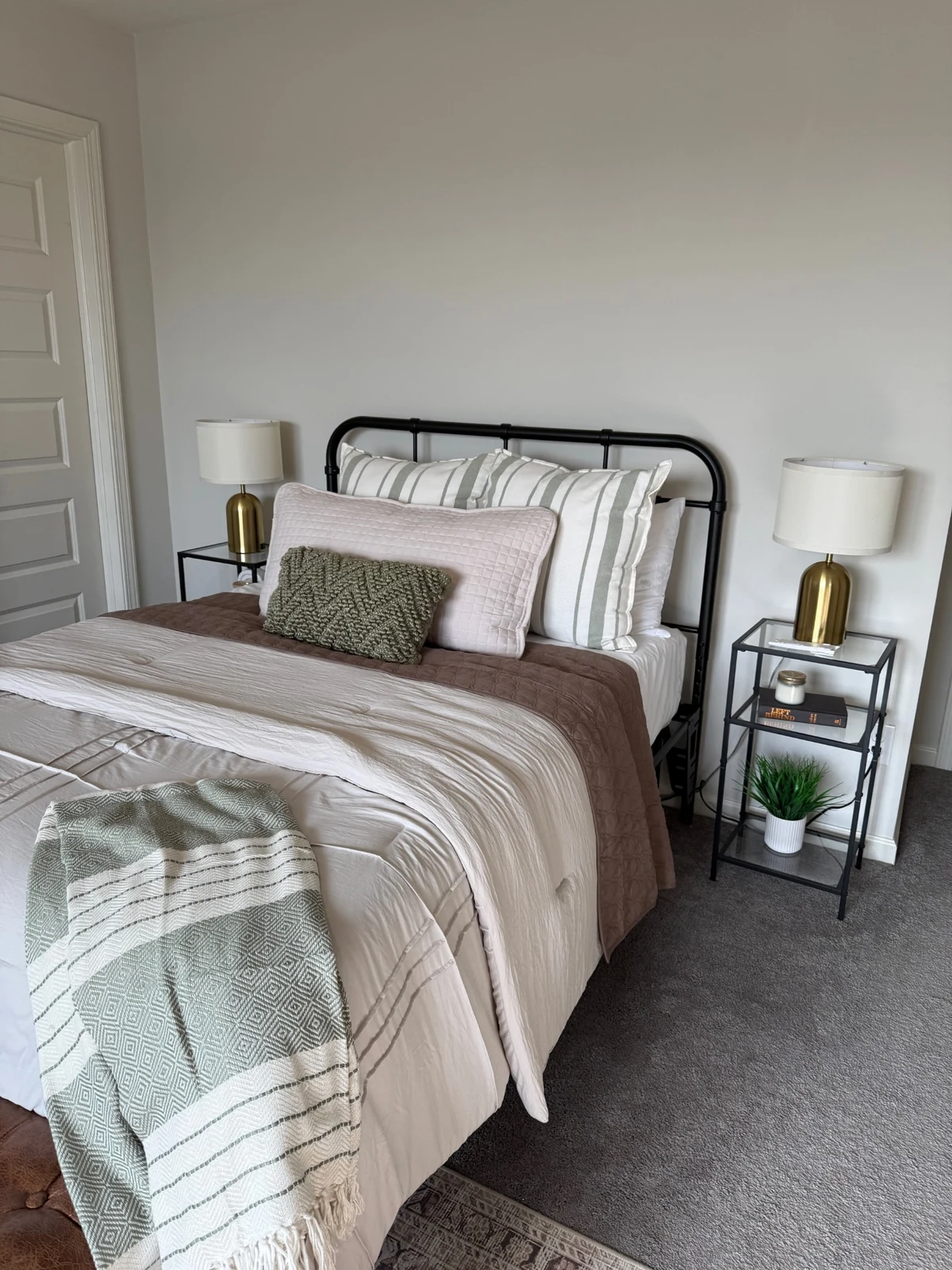Finished guest room with black metal bed, neutral bedding and brass lamps